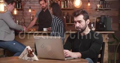年轻的帅哥在老式咖啡店里放松时，在笔记本电脑上输入一条信息